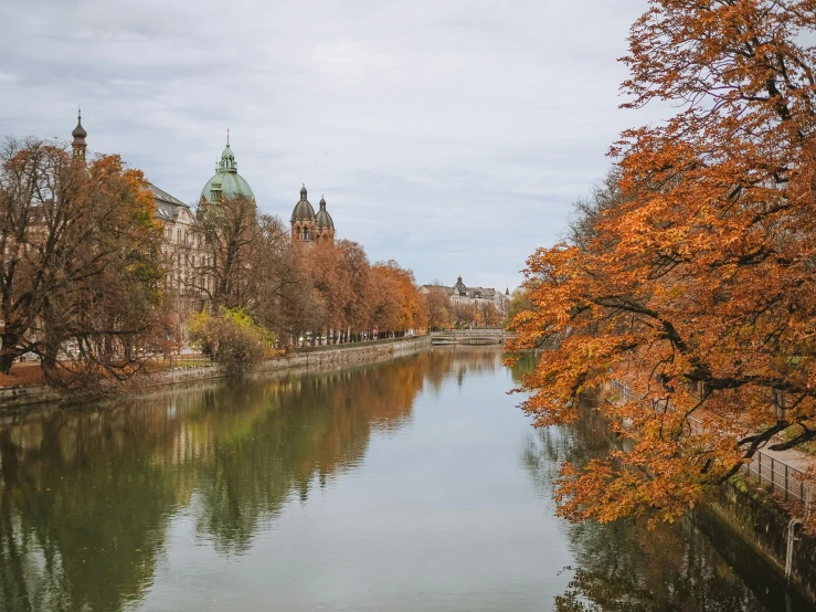 a river running through a city next to tall buildings, a photo, by Emma Andijewska, pexels contest winner, orange and brown leaves for hair, hannover, royal palace near the lake, thumbnail