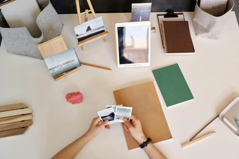 a person sitting at a table holding a polaroid camera, visual art, minimalist desk, various items, detailed product image, square pictureframes