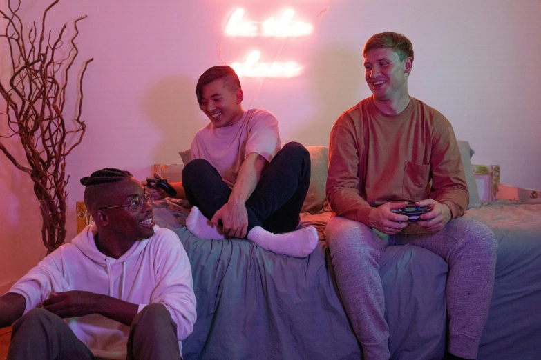 a couple of men sitting on top of a bed, an album cover, inspired by Russell Dongjun Lu, pexels, gaming room in 2 0 4 0, photograph of three ravers, good friends, bisexual lighting