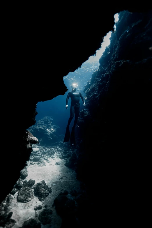 a person standing inside of a cave next to a body of water, by Daren Bader, coral sea bottom, man in dark blue full body suit, maui, looking downwards