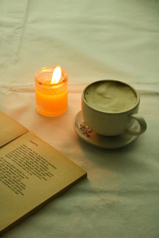 an open book sitting on top of a table next to a cup of coffee, romanticism, holding a candle, light tan, light orange mist, vanilla