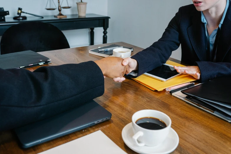 two people shaking hands over a wooden table, by Carey Morris, pexels contest winner, sitting in office, table in front with a cup, professional branding, background image