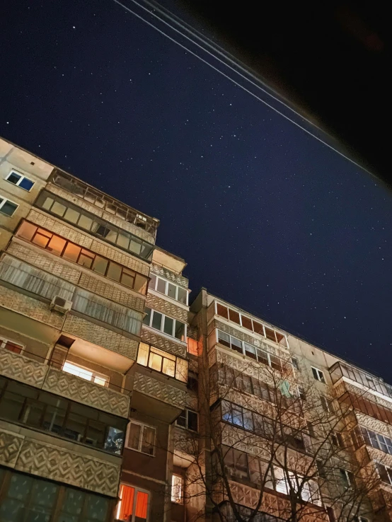 a tall building is lit up at night, by Kristian Zahrtmann, unsplash contest winner, hyperrealism, soviet suburbs, stars, low angle uhd 8 k, shot on iphone 1 3 pro