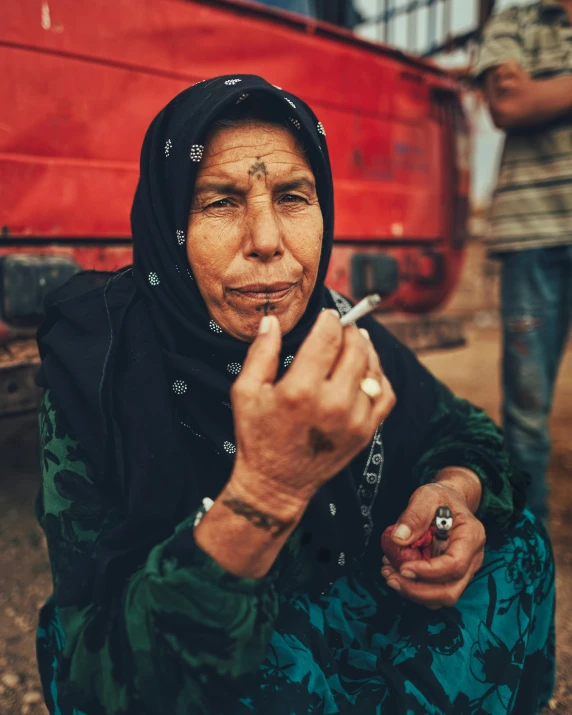 a woman sitting on the ground smoking a cigarette, by Matija Jama, hurufiyya, from egypt, lgbtq, old woman, cannabis
