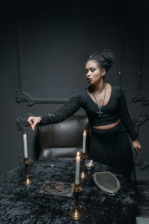 a woman standing in front of a table with candles, inspired by Elsa Bleda, renaissance, victorian goth, threatening pose, photo of a black woman, witchcore