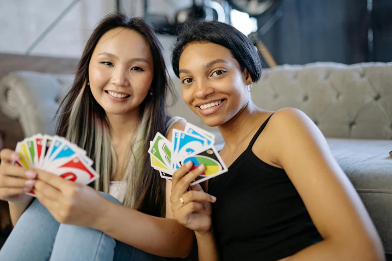 two women sitting on a couch holding playing cards, inspired by Aquirax Uno, unsplash, square, multicoloured, teenager hangout spot, ying and yang