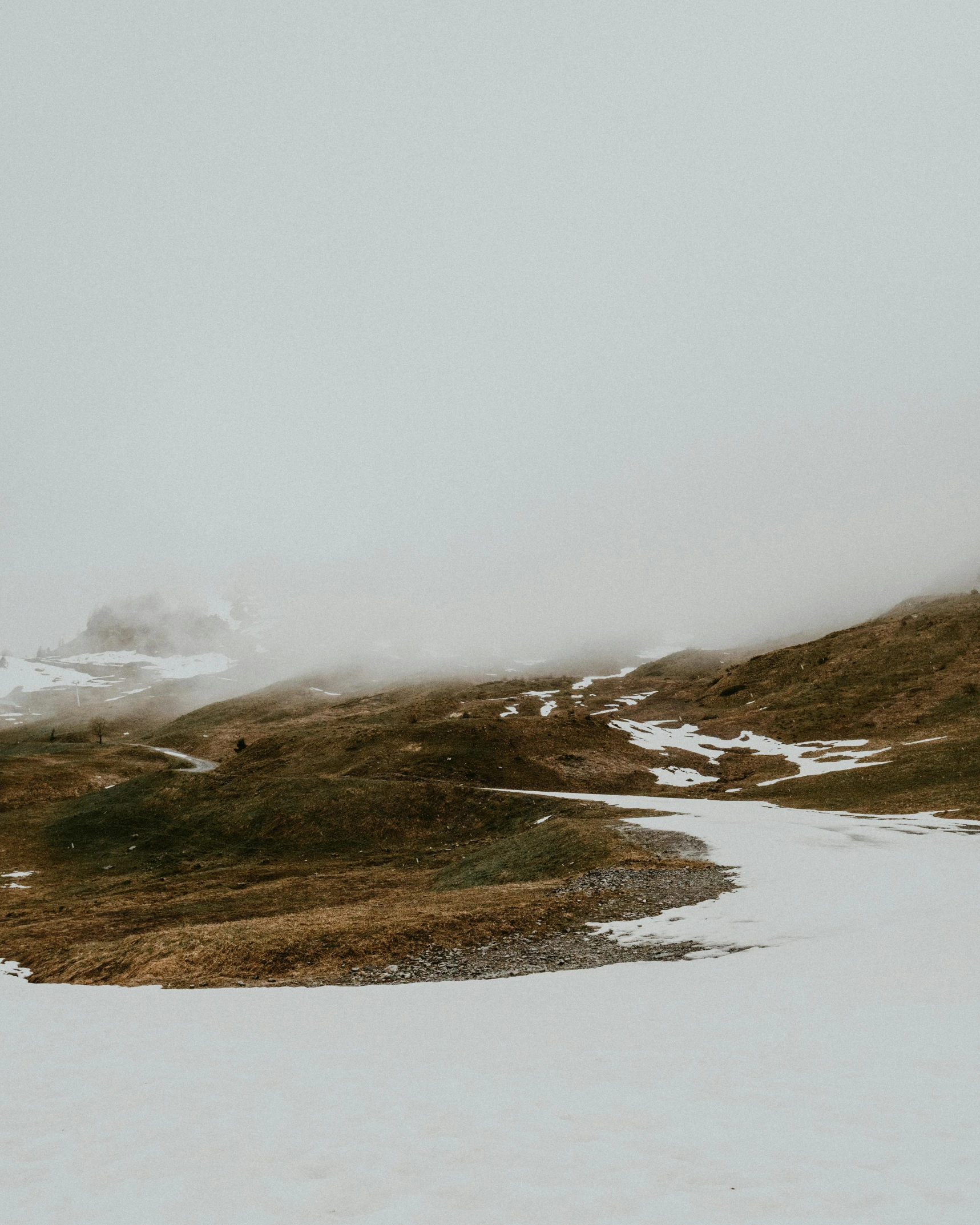 a man riding skis down a snow covered slope, by Emma Andijewska, unsplash contest winner, rainy and foggy, an icelandic landscape, spring winter nature melted snow, on the top of a hill