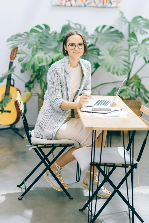 a woman sitting at a table with a laptop, wearing white suit and glasses, next to a plant, trending arstationhq, sitting on designer chair