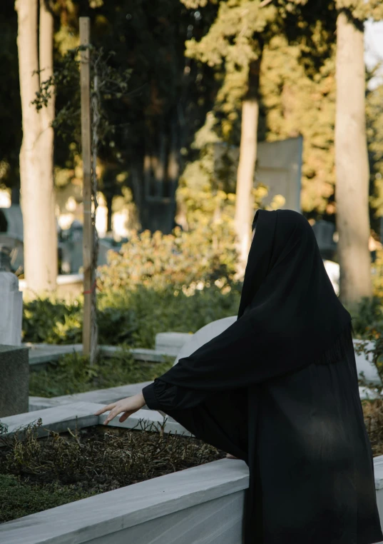 a woman in a black robe standing in a cemetery, an album cover, inspired by Modest Urgell, unsplash contest winner, realism, man sitting facing away, burka, ignant, ( ( theatrical ) )