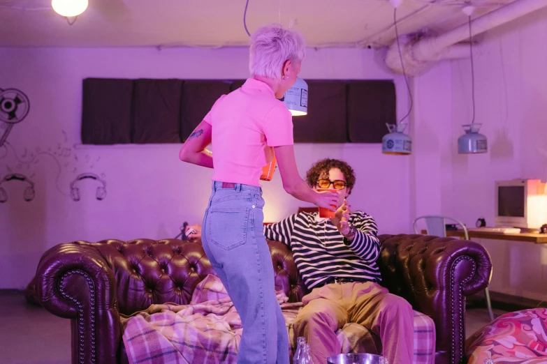 a woman standing next to a man sitting on a couch, by Helen Stevenson, pexels, rococo, soft neon purple lighting, lil peep, performance art, tickle fight in the death tent