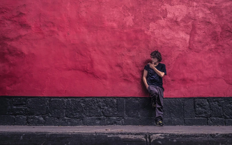 a man leaning against a red wall talking on a cell phone, an album cover, inspired by Steve McCurry, pexels contest winner, street art, tlaquepaque, panoramic view of girl, homeless, red haze