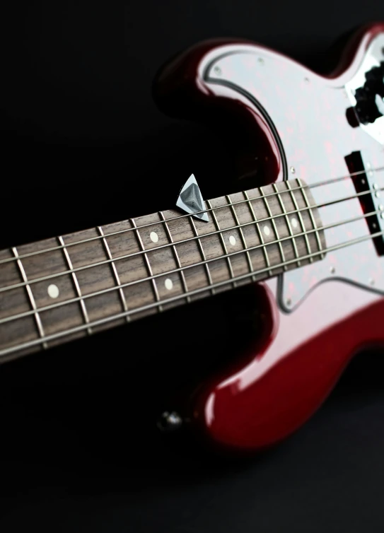 a red bass guitar sitting on top of a black surface, spiky, wine-red and grey trim, detail shot, stingray