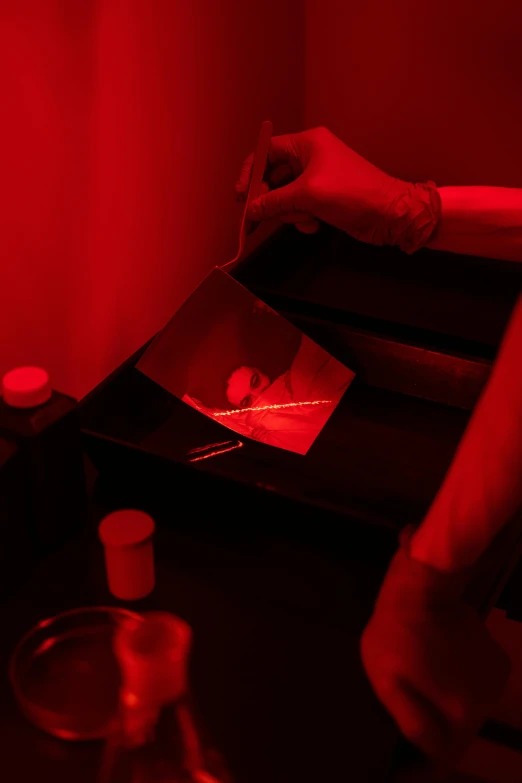 a person sitting at a table in front of a red light, a silk screen, holography, image apothecary, spraying blood, in a red dish, darkroom