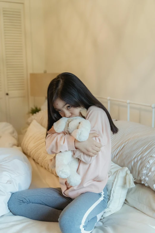 a woman sitting on a bed holding a teddy bear, by Tan Ting-pho, trending on reddit, woman crying, low quality photo, soft colors, black haired girl wearing hoodie