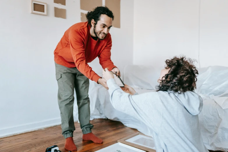 a man standing next to a woman on a bed, pexels contest winner, arbeitsrat für kunst, red shirt brown pants, repairing the other one, background image, furniture overturned