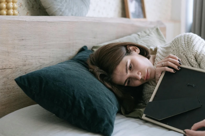 a woman laying on a bed with a laptop, a picture, inspired by Elsa Bleda, trending on pexels, happening, sad prisoner holding ipad, curled up on a book, woman holding sign, exhausted face close up