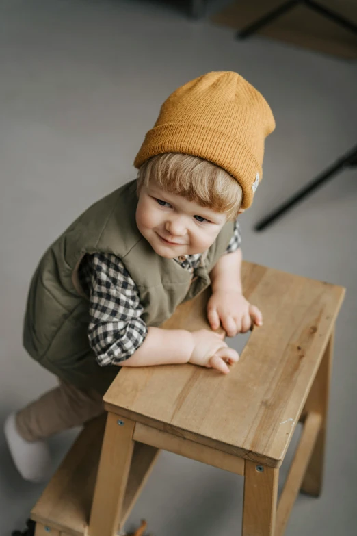 a little boy sitting on top of a wooden stool, trending on pexels, beanie, muted brown yellow and blacks, professionally assembled, bumpy