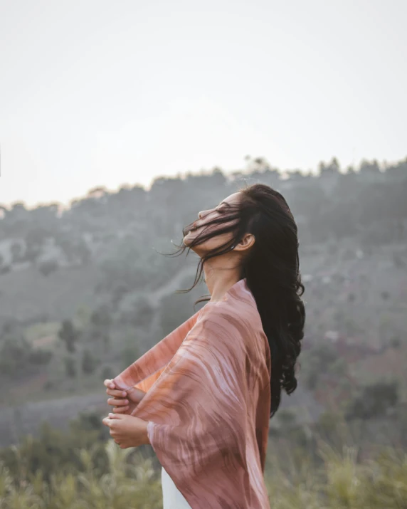 a woman standing on top of a lush green field, an album cover, inspired by Ren Hang, trending on unsplash, happening, wearing a scarf, pink mist, wearing brown robes, candid portrait photo