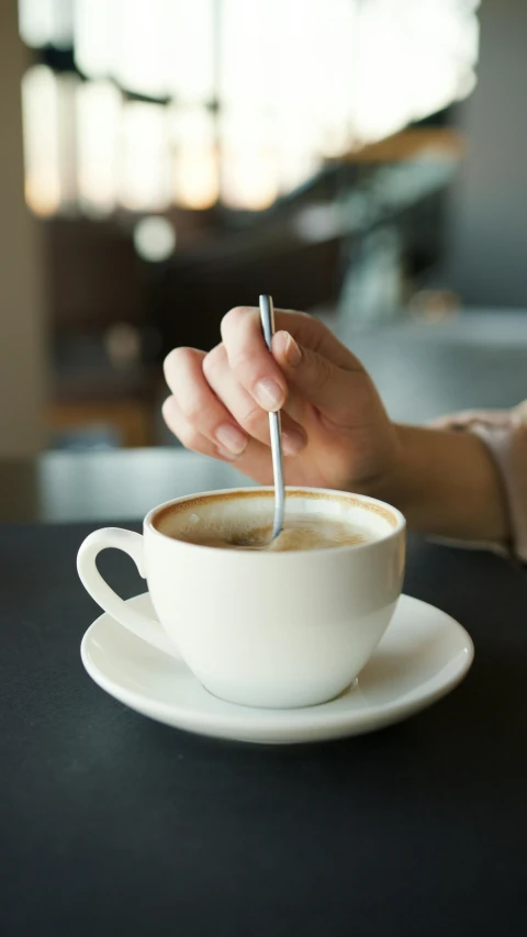 a person sitting at a table with a cup of coffee, spoon placed, square, thumbnail, vanilla