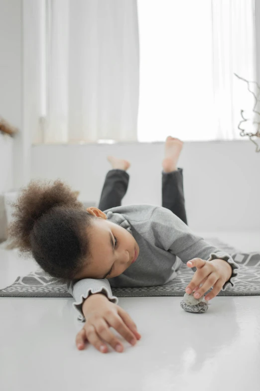 a little girl laying on her stomach on the floor, vibrating, the rock is a potato alarm clock, full product shot, grey