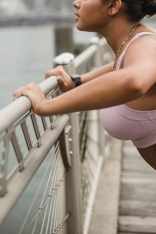 a woman leaning on a railing next to a body of water, happening, detailed sports bra, half turned around, connectivity, 6 : 3 0 am