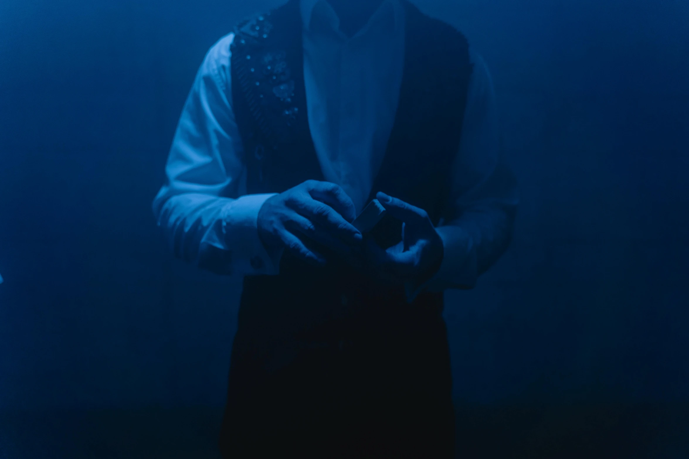 a man in a tuxedo holding a camera, by Elsa Bleda, unsplash, surrealism, cinematic blue lighting, still from a music video, a seance, light from bottom