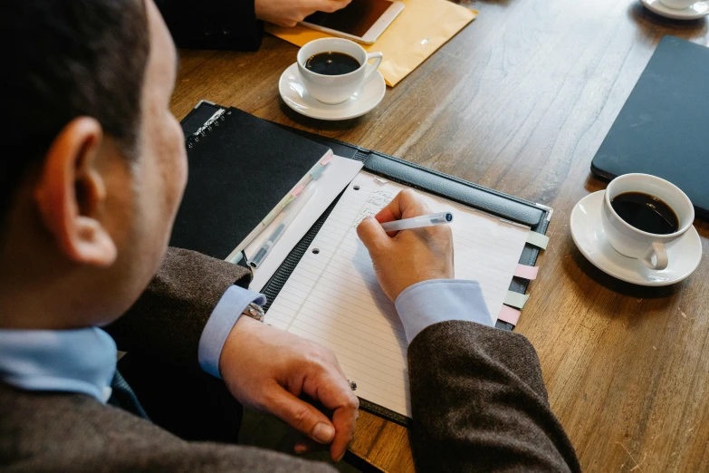 a man sitting at a table writing on a piece of paper, by Carey Morris, pexels contest winner, business meeting, background image, te pae, high angle shot