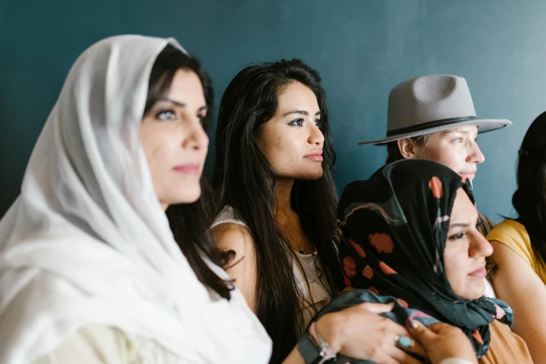 a group of women sitting next to each other, by Maryam Hashemi, trending on unsplash, hurufiyya, wearing white silk hood, migrant mother, looking to his side, wearing a hat