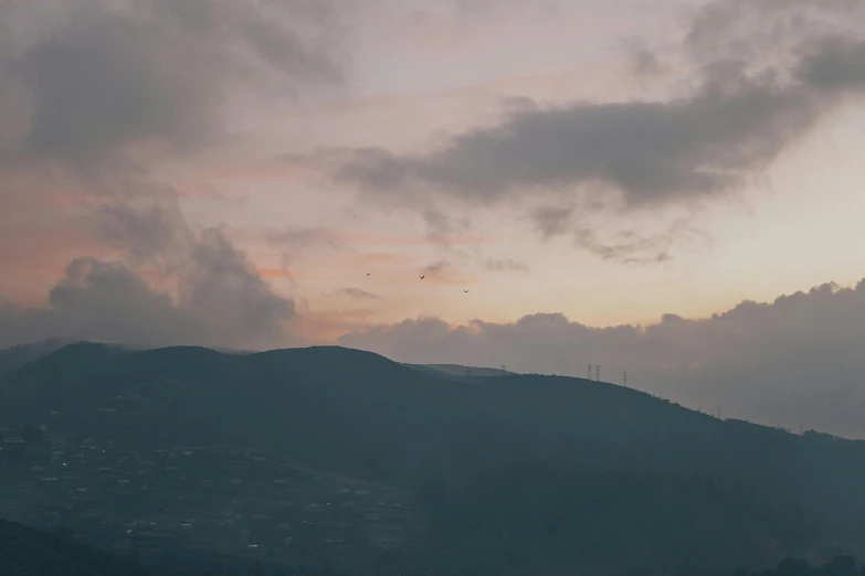 a person flying a kite on top of a lush green hillside, a picture, by Elsa Bleda, happening, cloudy sunset, distant town in valley and hills, cinematic shot ar 9:16 -n 6 -g, pink and grey clouds