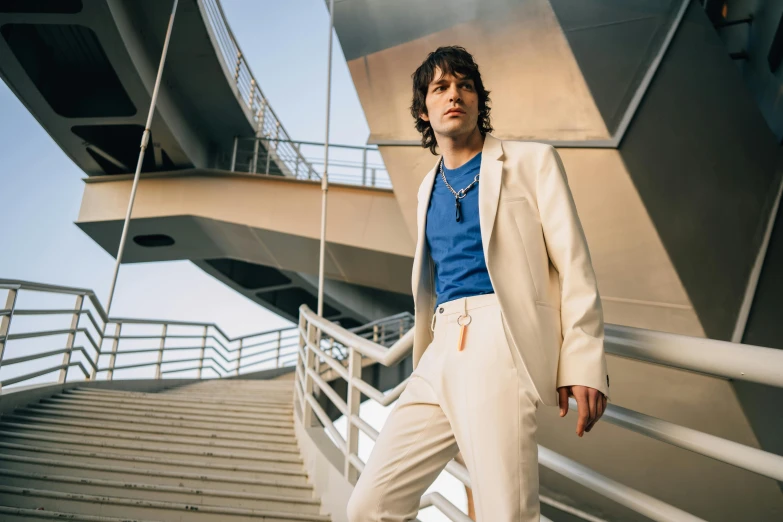 a man in a suit standing on a set of stairs, an album cover, by Raphaël Collin, pexels contest winner, finn wolfhard, on a bridge, wearing white suit, blue gold suit