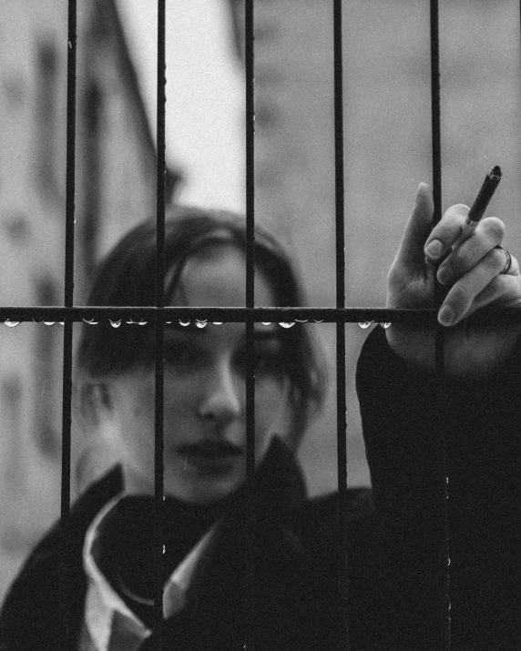 a black and white photo of a woman smoking a cigarette, inspired by Elsa Bleda, unsplash, behind bars, artist unknown, looking at you, teenage girl