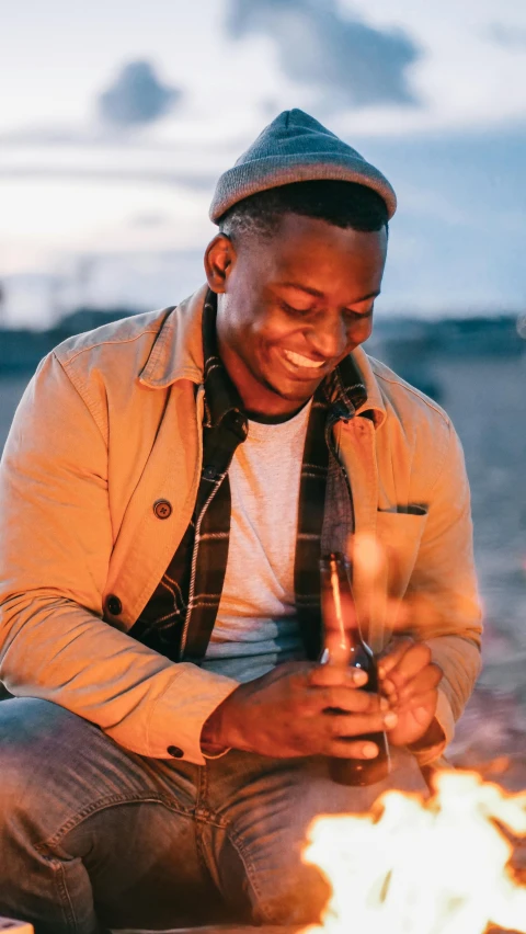 a man sitting next to a fire on a beach, an album cover, pexels contest winner, brown skin man with a giant grin, profile image, holding a torch, instagram photo