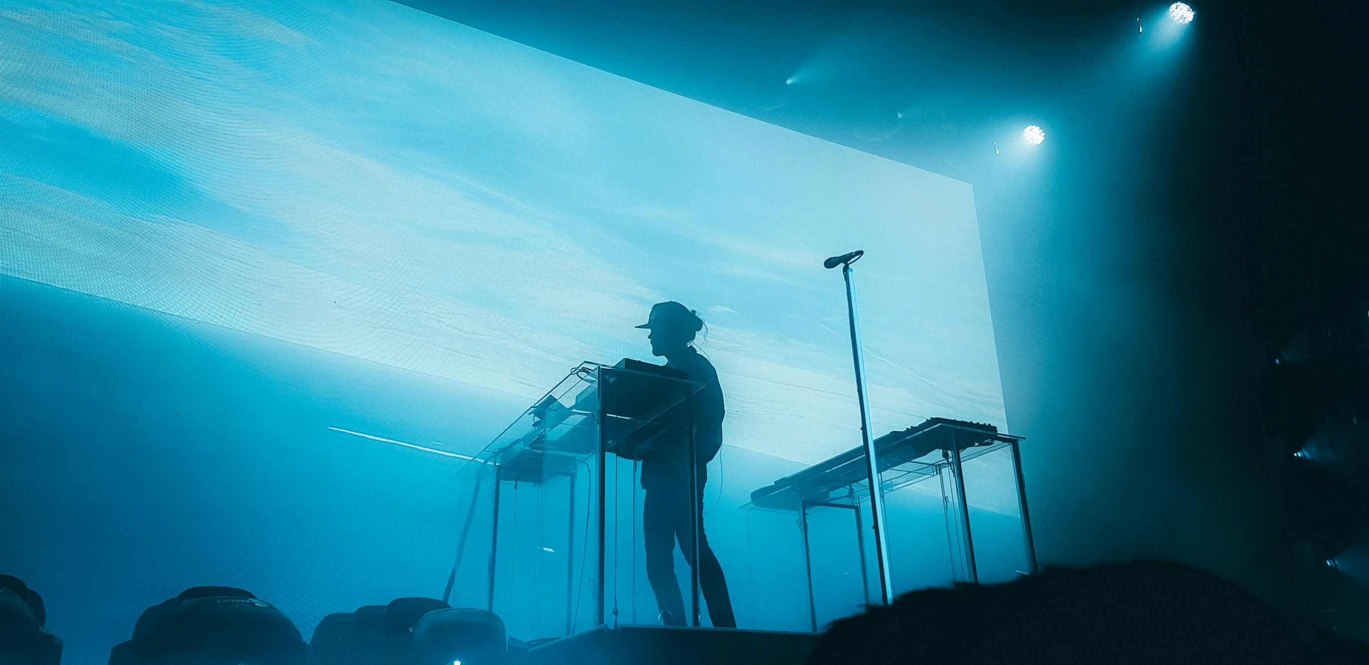 a man standing at a podium in front of a screen, a hologram, inspired by Mike Winkelmann, unsplash contest winner, bauhaus, sitting in his throne underwater, keyboardist, kendrick lamar, cyan dimensional light