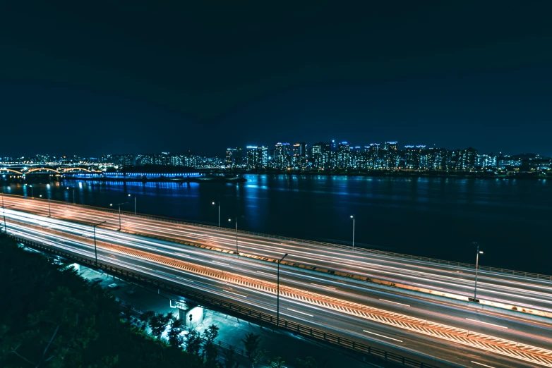 an aerial view of a city at night, by Jang Seung-eop, pexels contest winner, happening, freeway, the sea seen behind the city, fast shutter speed, plain background