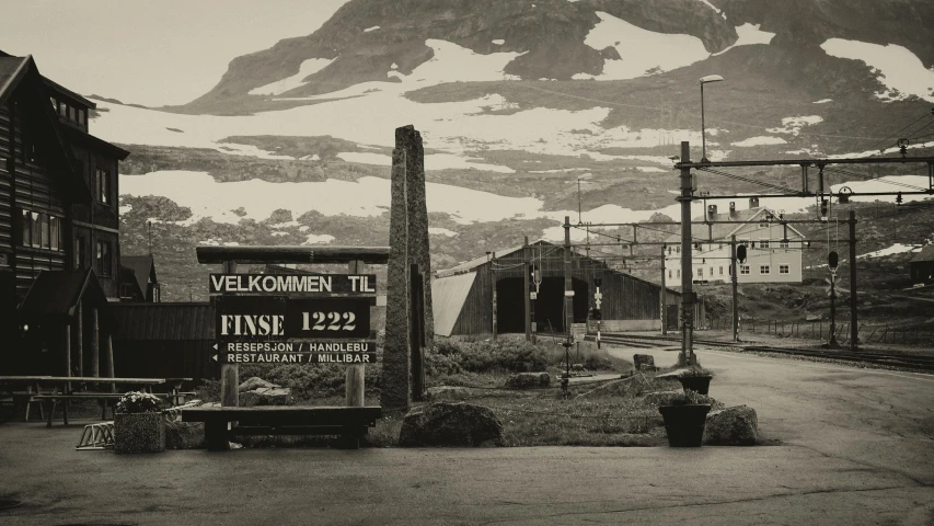 a black and white photo of a town with a mountain in the background, inspired by Einar Hakonarson, pexels contest winner, fluxus, entrance to 1900's mine, old signs, 1981 photograph, bus station