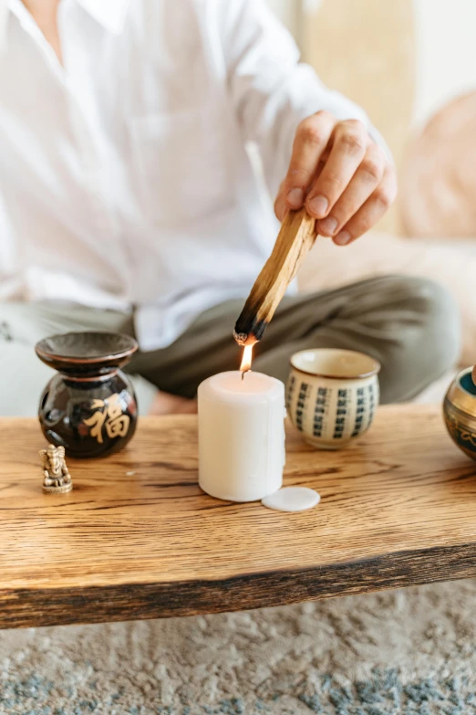 a woman lighting a candle on top of a wooden table, a still life, inspired by Kanō Shōsenin, trending on unsplash, mingei, made of glowing wax and ceramic, white, meditation, japanese collection product