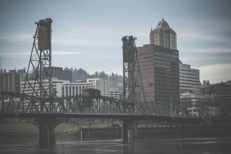 a bridge over a body of water with a city in the background, a photo, by Jason Felix, pexels contest winner, portland oregon, tall metal towers, faded and dusty, commercial banner