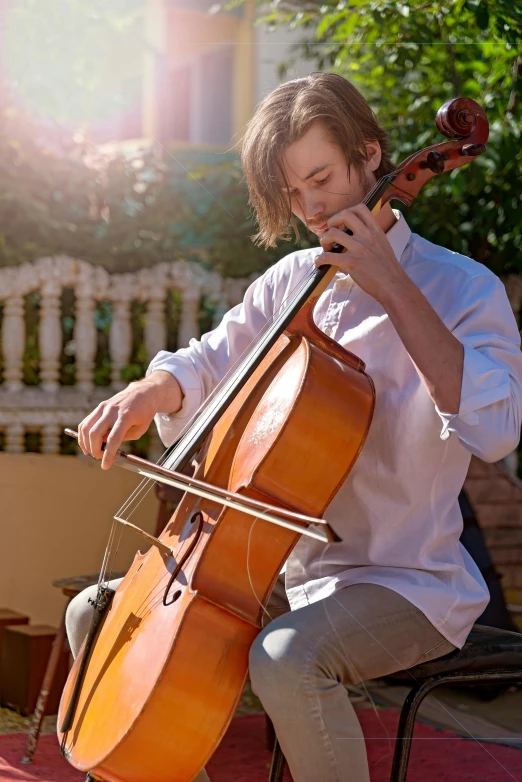 a man sitting on a chair playing a cello, in the sun, profile image, australian, 2 2 years old