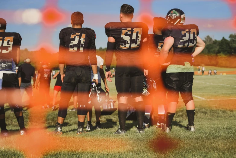 a group of young men standing on top of a field, by Matt Cavotta, pexels contest winner, football armor, orange and black, shallow depth of fielf, ilustration