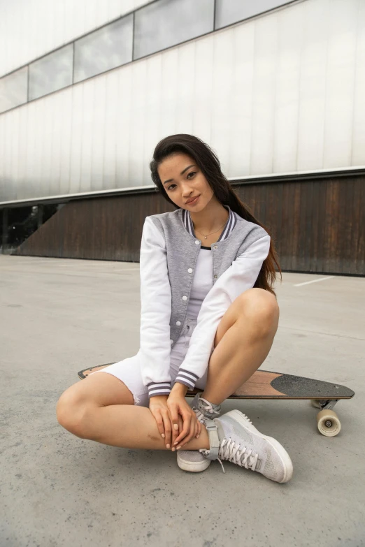 a woman sitting on a skateboard in front of a building, wearing a bomber jacket, white and silver, tennis wear, 5 0 0 px models