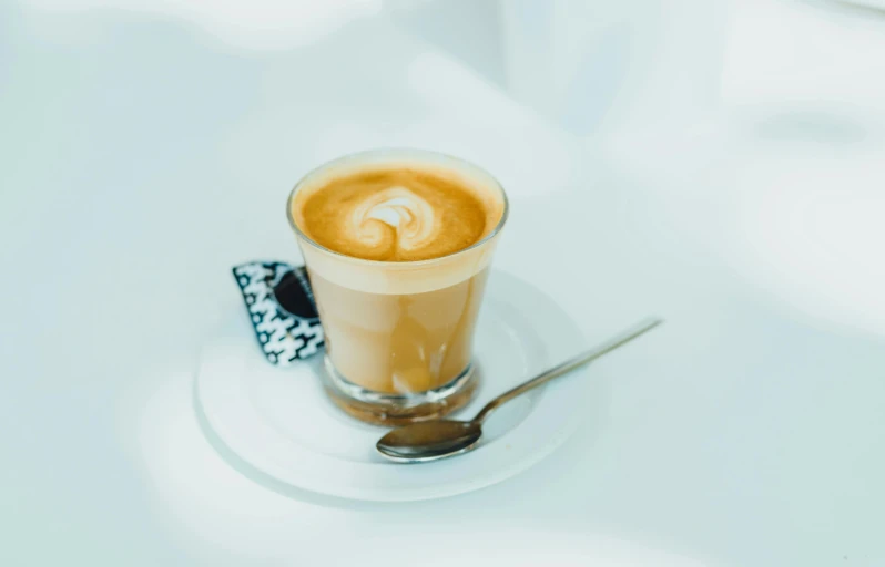 a cup of coffee on a saucer with a spoon, by Lee Loughridge, trending on unsplash, glass of milk, on a white table, aussie baristas, high quality photo