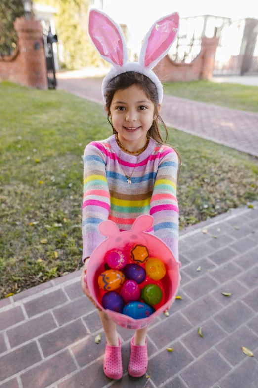 a little girl in bunny ears holding a basket of easter eggs, by Lilia Alvarado, pexels contest winner, candy colors, casually dressed, instagram post, striped