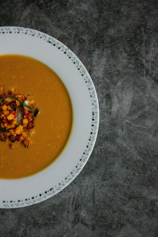 a bowl of soup sitting on top of a table, a portrait, unsplash, corn, on grey background, caramel, chile