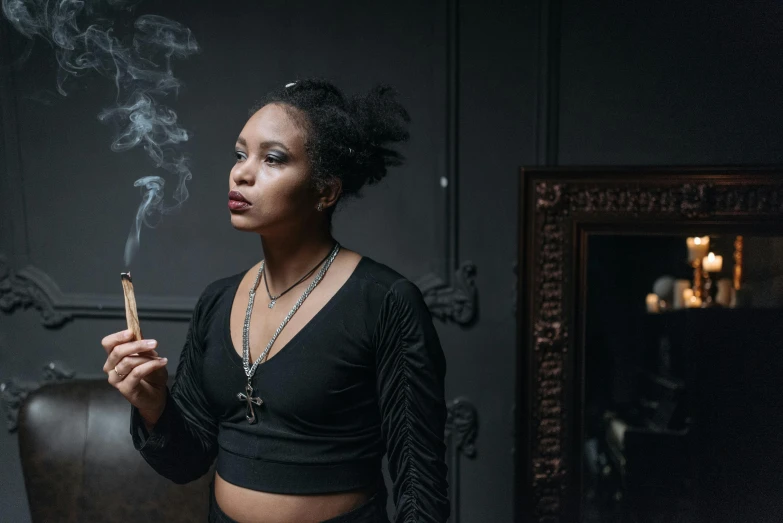 a woman in a black top smokes a cigarette, inspired by Carrie Mae Weems, pexels contest winner, black arts movement, holding grimoire, standing in a dimly lit room, a young female shaman, doja cat