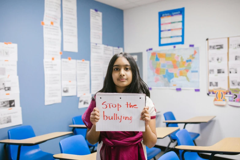 a girl holding up a sign in a classroom, trending on unsplash, bullying, hindu, usa-sep 20, portrait n - 9