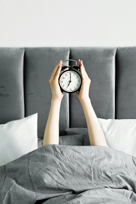 a person laying in bed holding an alarm clock, grey, premium, multiple stories, tall