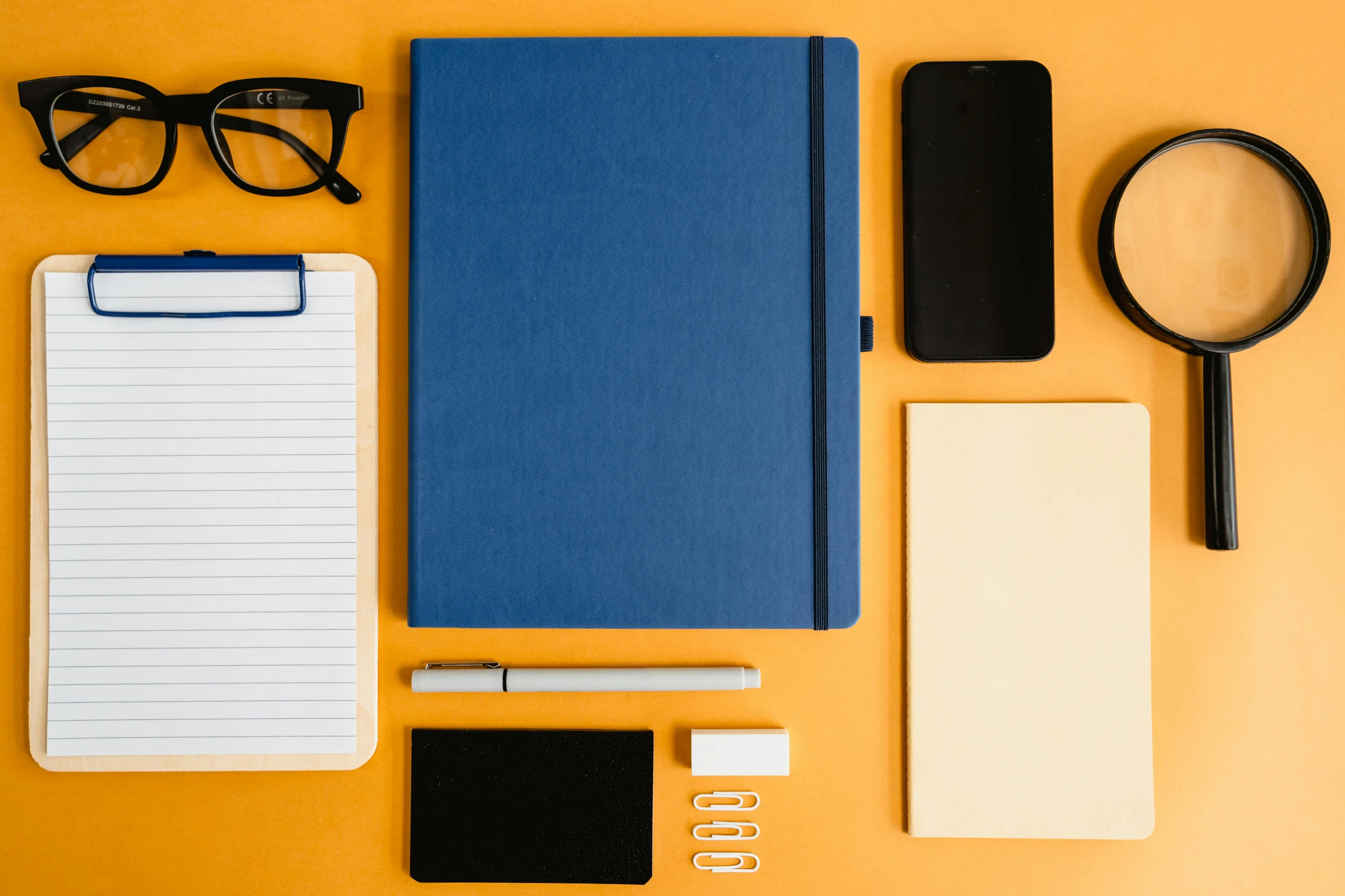 a variety of office supplies laid out on a yellow surface, trending on pexels, minimalism, dark blue + dark orange, holding notebook, waist - up, full device