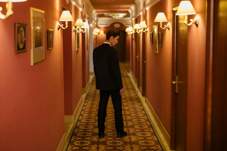 a man in a suit is walking down a hallway, an album cover, inspired by Raymond Leech, unsplash, happening, hotel room, hugh grant, ignant, worried