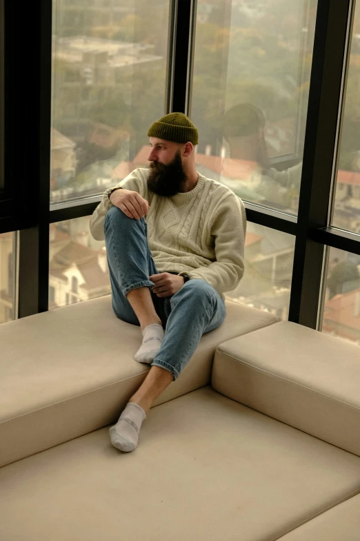 a man sitting on top of a couch next to a window, trending on pexels, hyperrealism, wearing beanie, fullbody photo, bearded, baris yesilbas