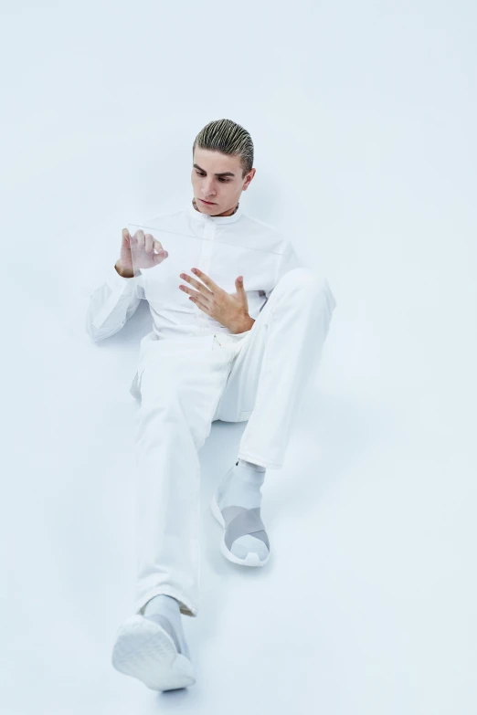 a man sitting on top of a white floor, an album cover, inspired by Adrian Zingg, white outfit, white sleeves, commercially ready, style of seb mckinnon